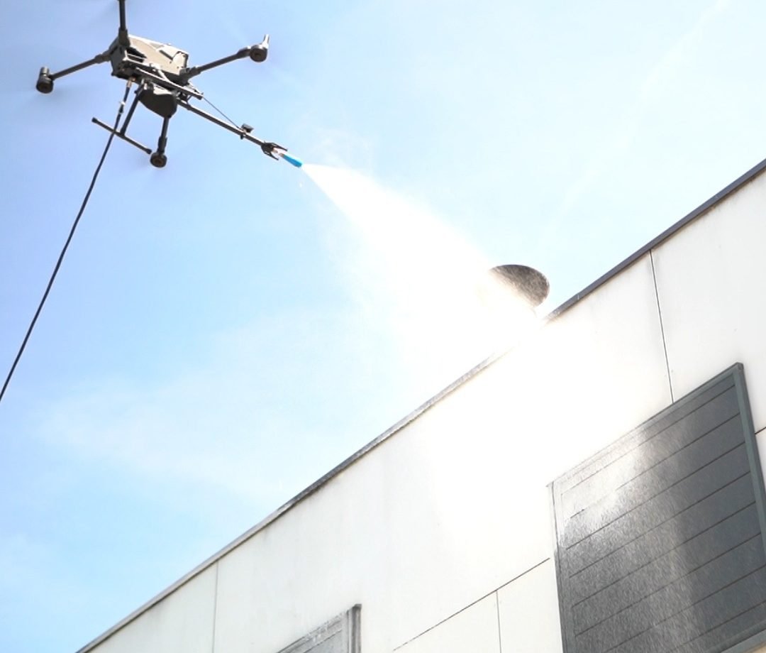 Drone de nettoyage projetant un jet sur le haut d'un bardage blanc