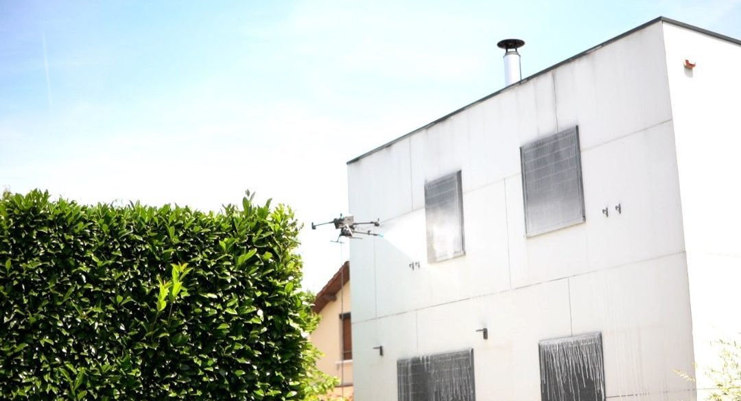 Maison au bardage blanc avec le drone de nettoyage en action devant la façade