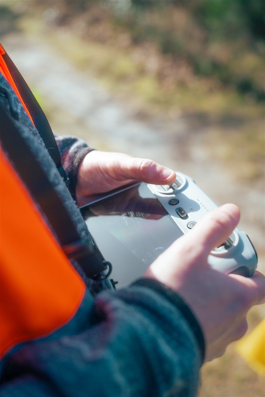 Mains d'un télépilote en gilet orange sur la radiocommande à écran d'un drone.